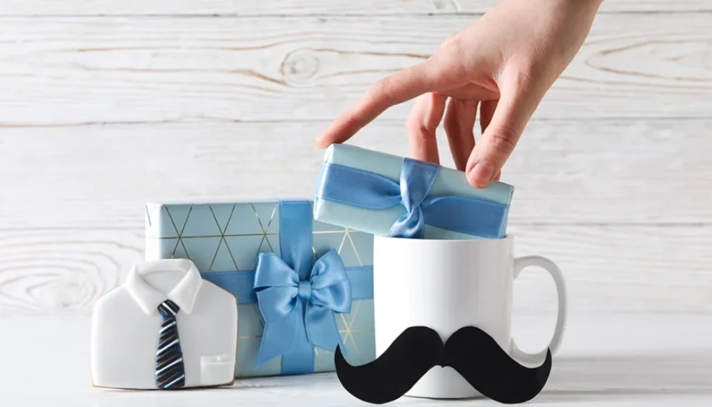 Prezent na Dzień Ojca – kubek z wąsem, upominki w niebieskim opakowaniu i ciastko w kształcie koszuli z krawatem
