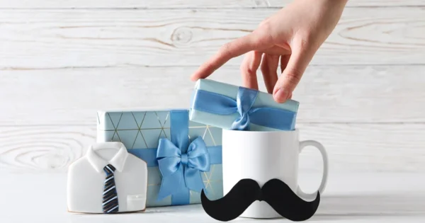 Prezent na Dzień Ojca – kubek z wąsem, upominki w niebieskim opakowaniu i ciastko w kształcie koszuli z krawatem