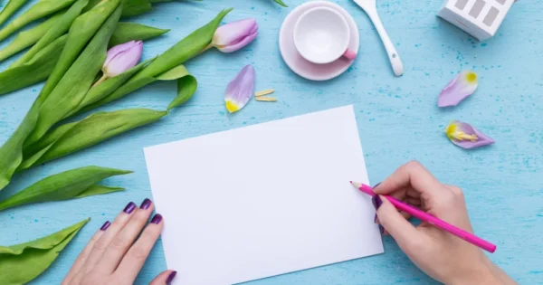 Kreatywne pisanie kartki na niebieskim tle z fioletowymi tulipanami i filiżanką kawy – pomysł na liścik z podziękowaniami